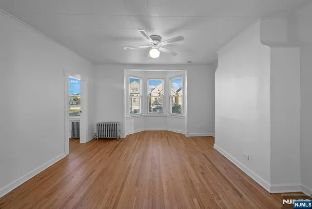an empty room with wooden floor chandelier fan and windows