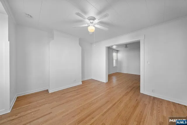 a view of an empty room with wooden floor and a ceiling fan