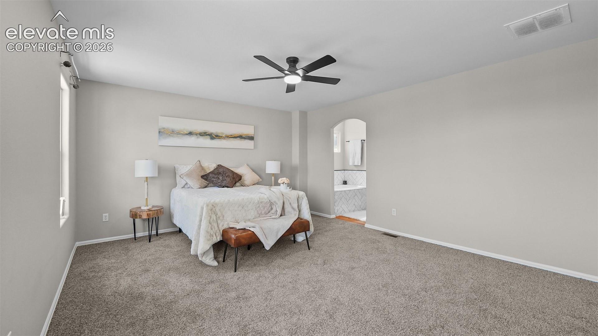 2044 Reed Grass Way Colorado Springs, CO 80915 - Photo 21 of 47 Spacious bedroom featuring vaulted ceilings, a ceiling fan with integrated lighting, soft gray carpeting, and an arched doorway opening to a bathroom with a tiled surround