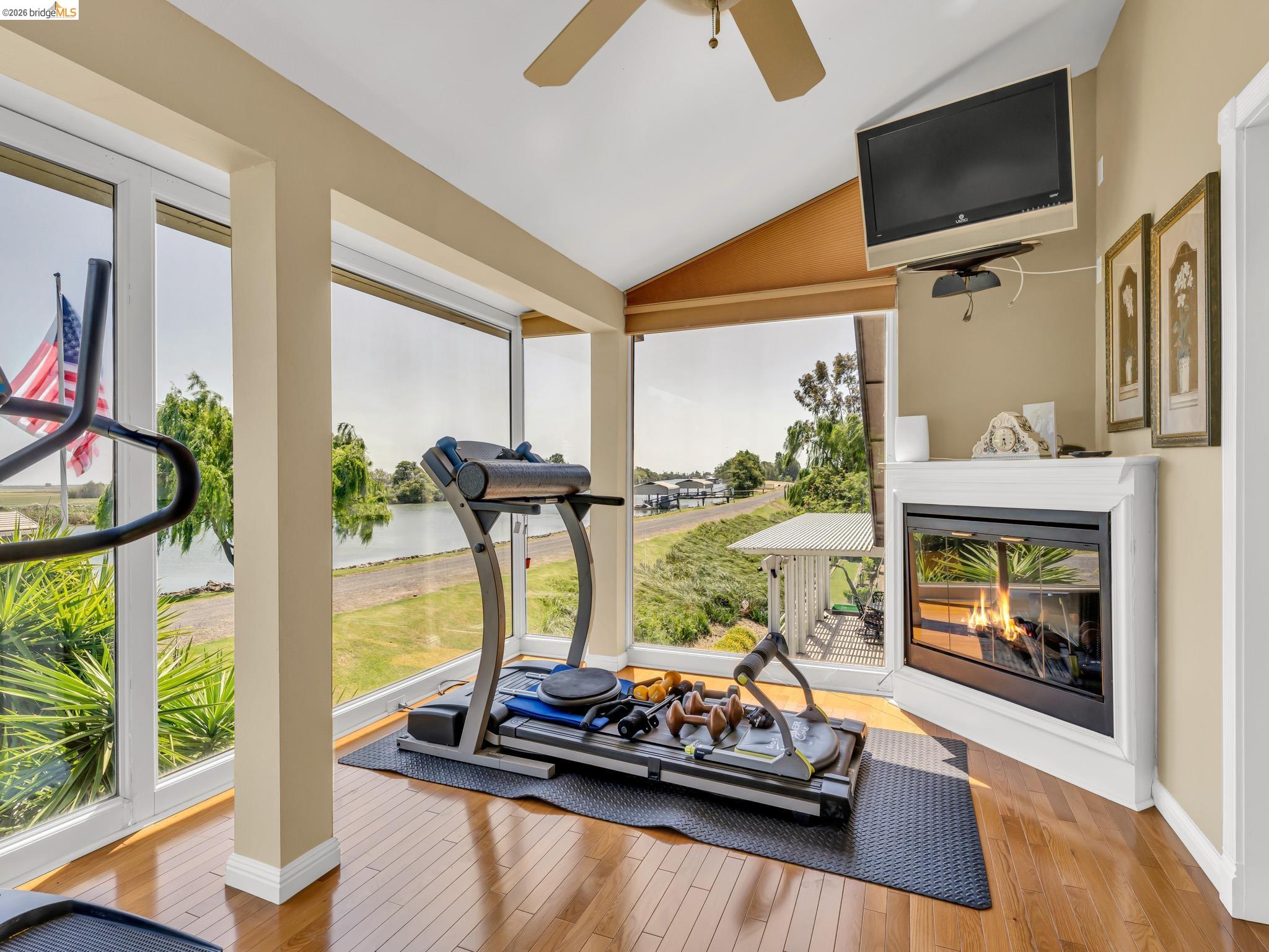 17035 Terminous Road Isleton, CA 95641 - Photo 31 of 48 Exercise room featuring a glass covered fireplace, lofted ceiling, light wood-type flooring, a ceiling fan, and healthy amount of natural light