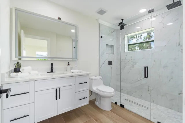 a bathroom with a toilet a sink a glass door a shower and a mirror