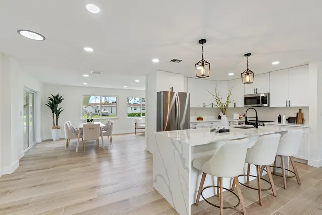 a kitchen with stainless steel appliances kitchen island granite countertop a dining table chairs and white cabinets