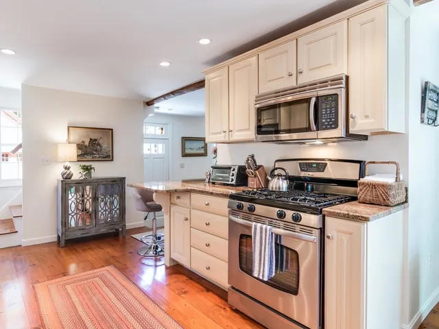 a kitchen with stainless steel appliances granite countertop a stove top oven a sink dishwasher and white cabinets with wooden floor