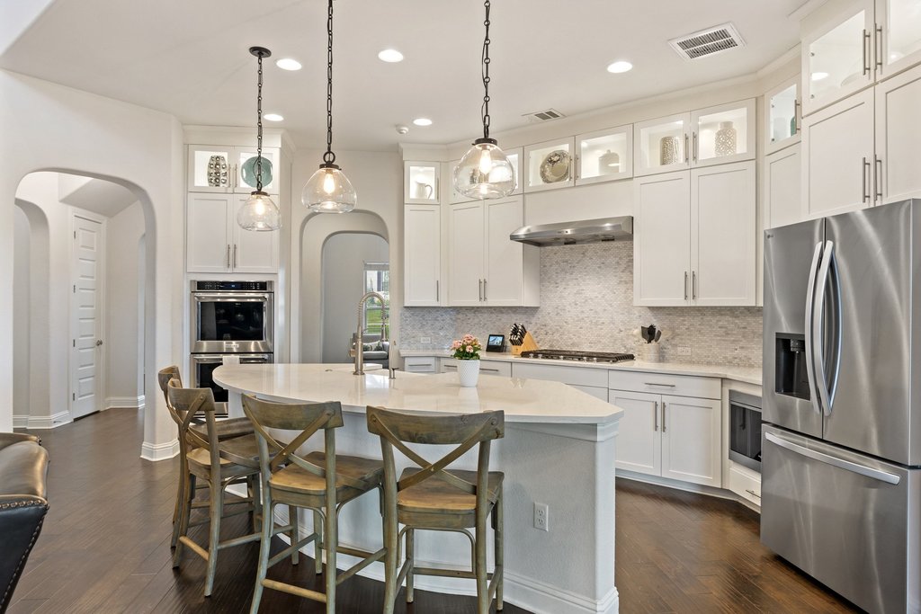 215 Lodestone Lane Austin, TX 78738 - Photo 5 of 40 White cabinetry, elegant pendant lighting, and a spacious kitchen island create a refined culinary atmosphere.