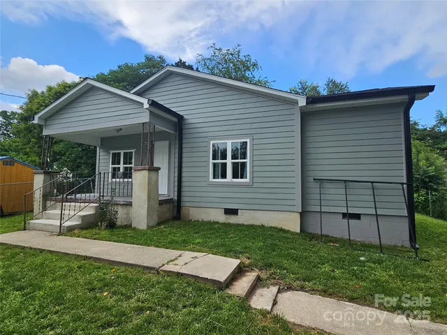 a view of a house with a yard plants and large tree