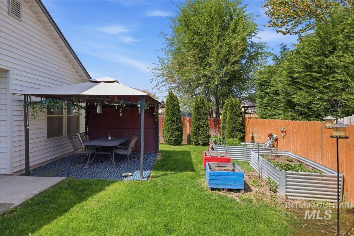 1068 Locksley Street Middleton, ID 83644 - Photo 30 of 30 Expansive backyard featuring a covered patio with a blue geometric-patterned outdoor rug, a lush green lawn, and multiple raised garden beds