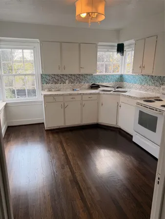 a kitchen with granite countertop a stove a sink and white cabinets with wooden floor next to windows