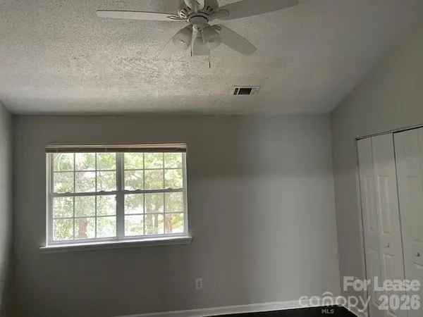 an empty room with chandelier fan and windows