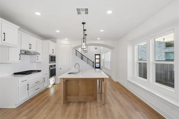 a large kitchen with stainless steel appliances kitchen island granite countertop a stove a refrigerator a sink and white cabinets with wooden floor