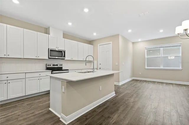 a kitchen with stainless steel appliances granite countertop a sink dishwasher a stove and white cabinets with wooden floor