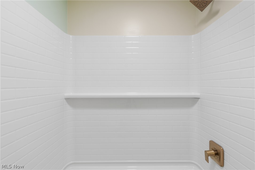 1075 Northeast River Road Lake Milton, OH 44429 - Photo 18 of 34 Shower enclosure featuring white subway tile surround, integrated shelving, and a brass-finish rain shower head with coordinating controls