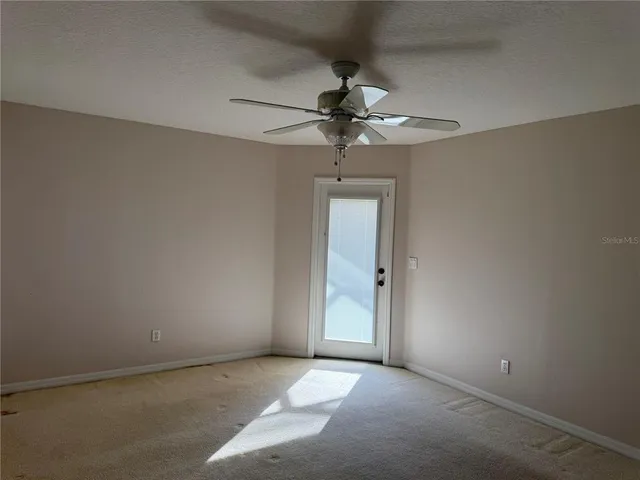 an empty room with a chandelier fan and windows