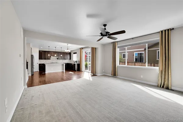 a view of a livingroom with a fireplace a ceiling fan a windows and a kitchen view