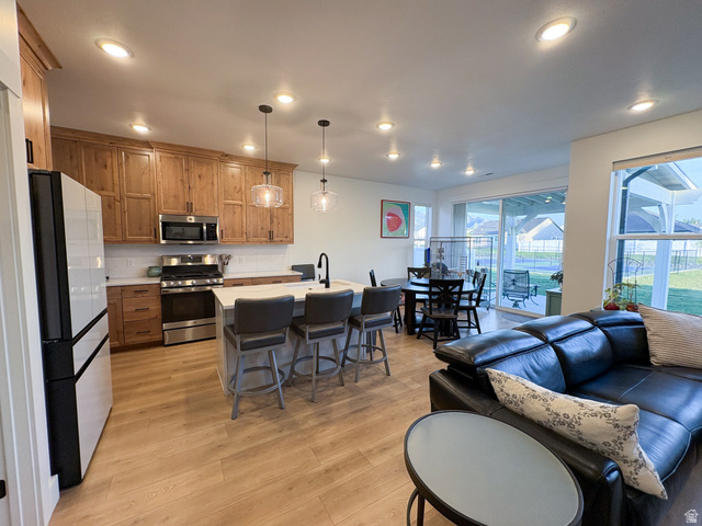 412 West 3025th Street South Logan, UT 84321 - Photo 18 of 34 Kitchen featuring a center island with sink, stainless steel appliances, a kitchen bar, wood finish cabinetry, and light wood-style floors