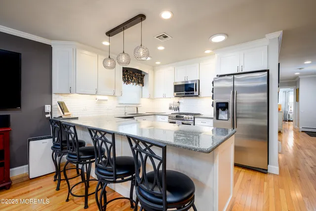 a kitchen with stainless steel appliances granite countertop a stove a refrigerator a kitchen island a dining table and chairs with wooden floor