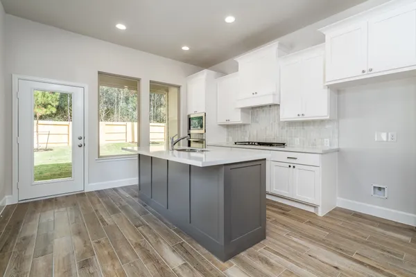a kitchen with granite countertop a stove a sink and white cabinets with wooden floor