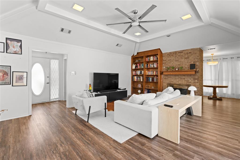 3506 Ruidoso Drive Arlington, TX 76017 - Photo 3 of 37 Spacious living area featuring wood-finish flooring, a vaulted ceiling with recessed lighting and a ceiling fan, a brick accent wall with a fireplace and wood mantel, and built-in wood shelving