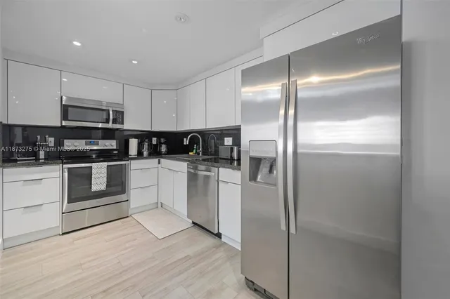 a kitchen with stainless steel appliances kitchen island granite countertop a refrigerator a sink and white cabinets