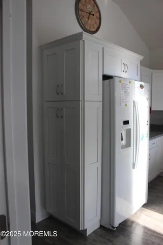 a view of a refrigerator in kitchen and an empty room with wooden floor