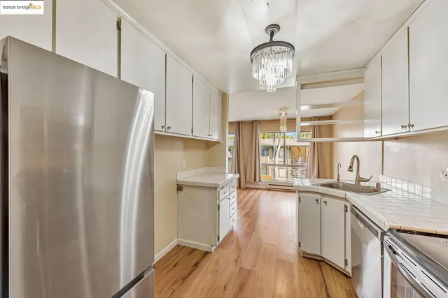 a kitchen with stainless steel appliances granite countertop a refrigerator a sink dishwasher a stove and white cabinets with wooden floor