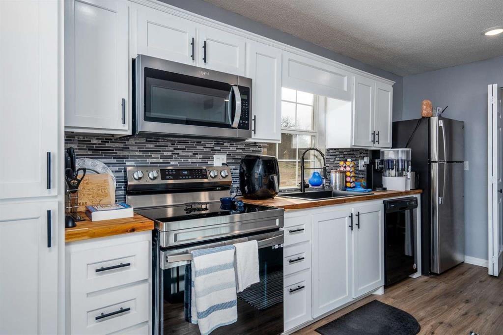 365 Co Road Stamford, TX 79553 - Photo 7 of 23 White cabinetry with matte black hardware, stainless steel appliances, wood-finish countertops, tiled backsplash, and wood-finish flooring
