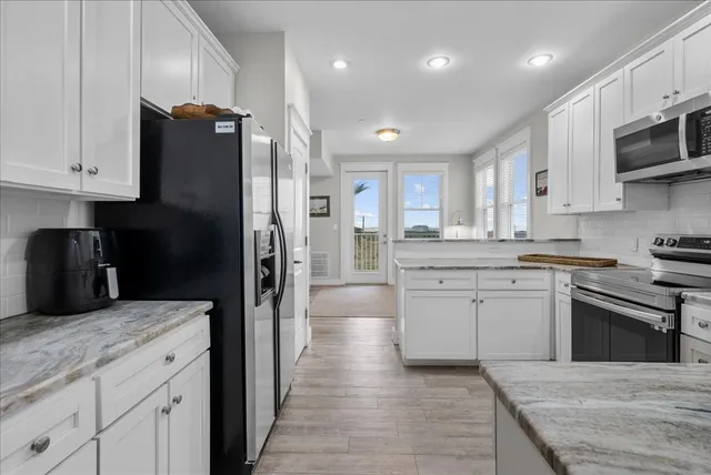 a kitchen with stainless steel appliances granite countertop a refrigerator a sink dishwasher a stove and white cabinets with wooden floor