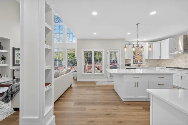 a large white kitchen with granite countertop a stove top oven a sink dishwasher and white cabinets with wooden floor