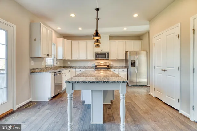 a kitchen with kitchen island granite countertop wooden floors white cabinets and stainless steel appliances