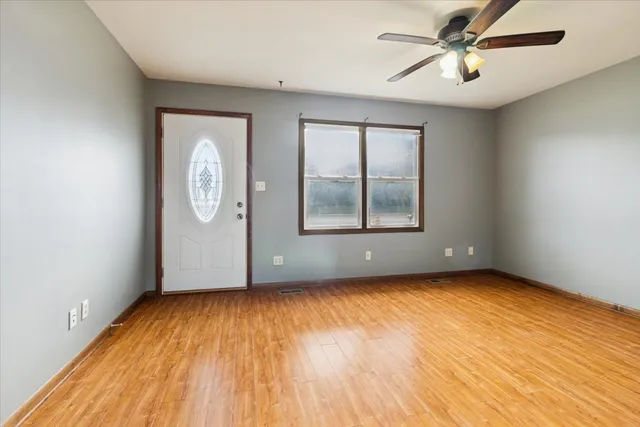 an empty room with wooden floor chandelier fan and windows
