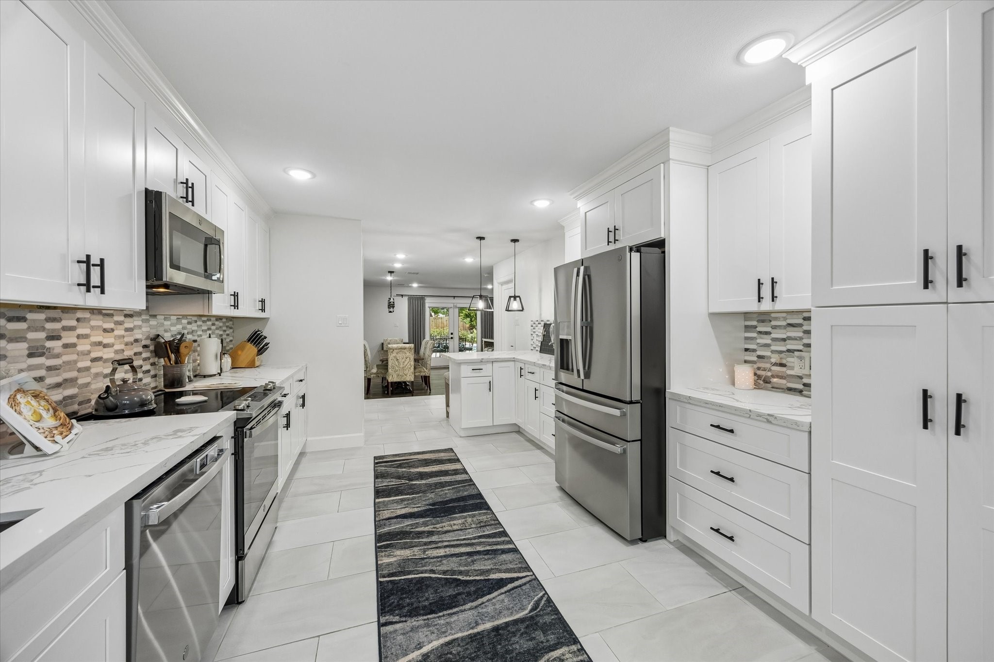1420 Indiana Street Houston, TX 77006 - Photo 13 of 31 This kitchen is modern and spacious, featuring sleek white cabinetry, stainless steel appliances, and a stylish backsplash. The open layout flows into a dining area, creating a perfect space for entertaining.