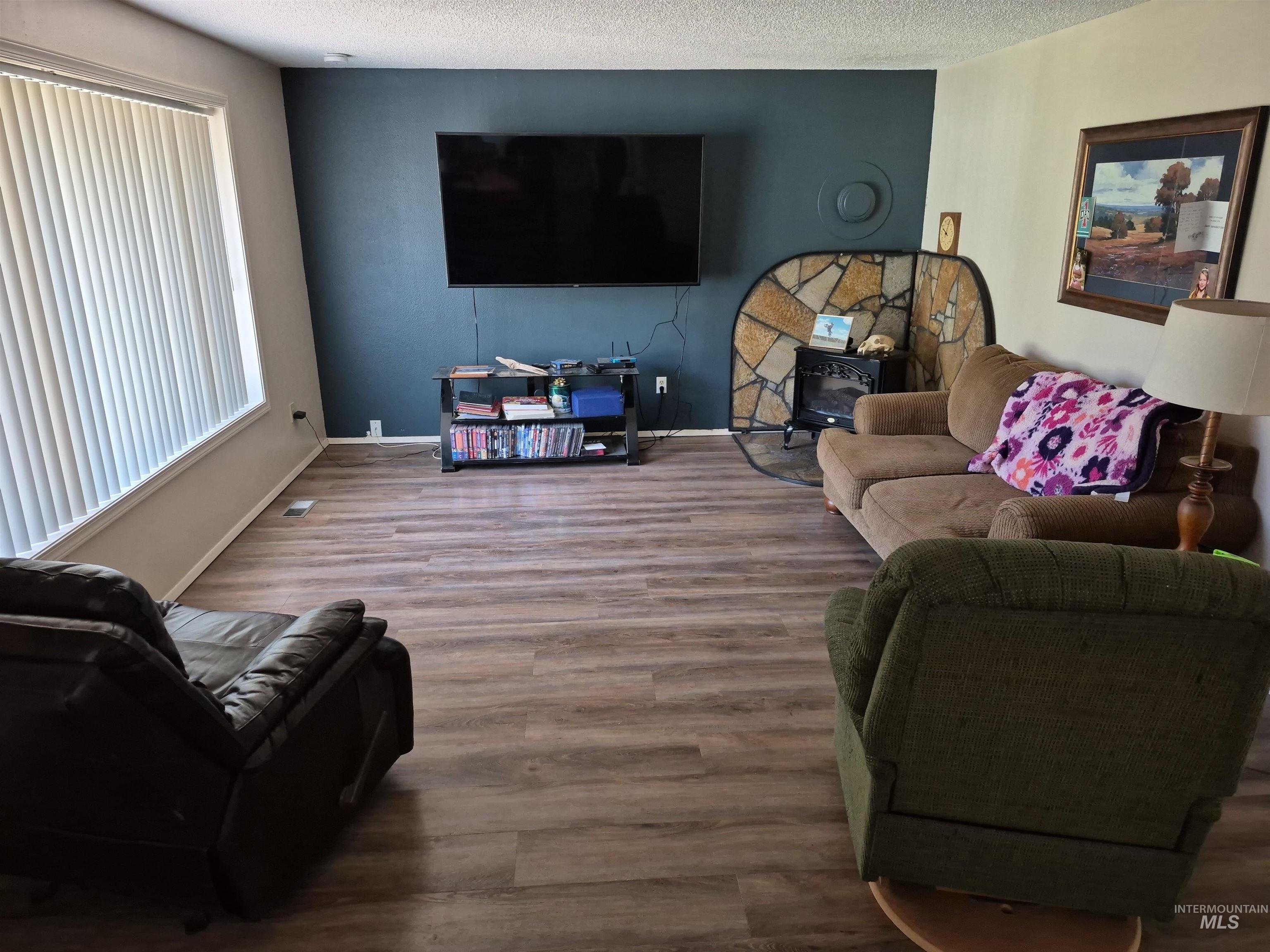 701 Wheeler Street Kendrick, ID 83537 - Photo 14 of 32 Living room featuring a wood stove, wood finished floors, and a textured ceiling