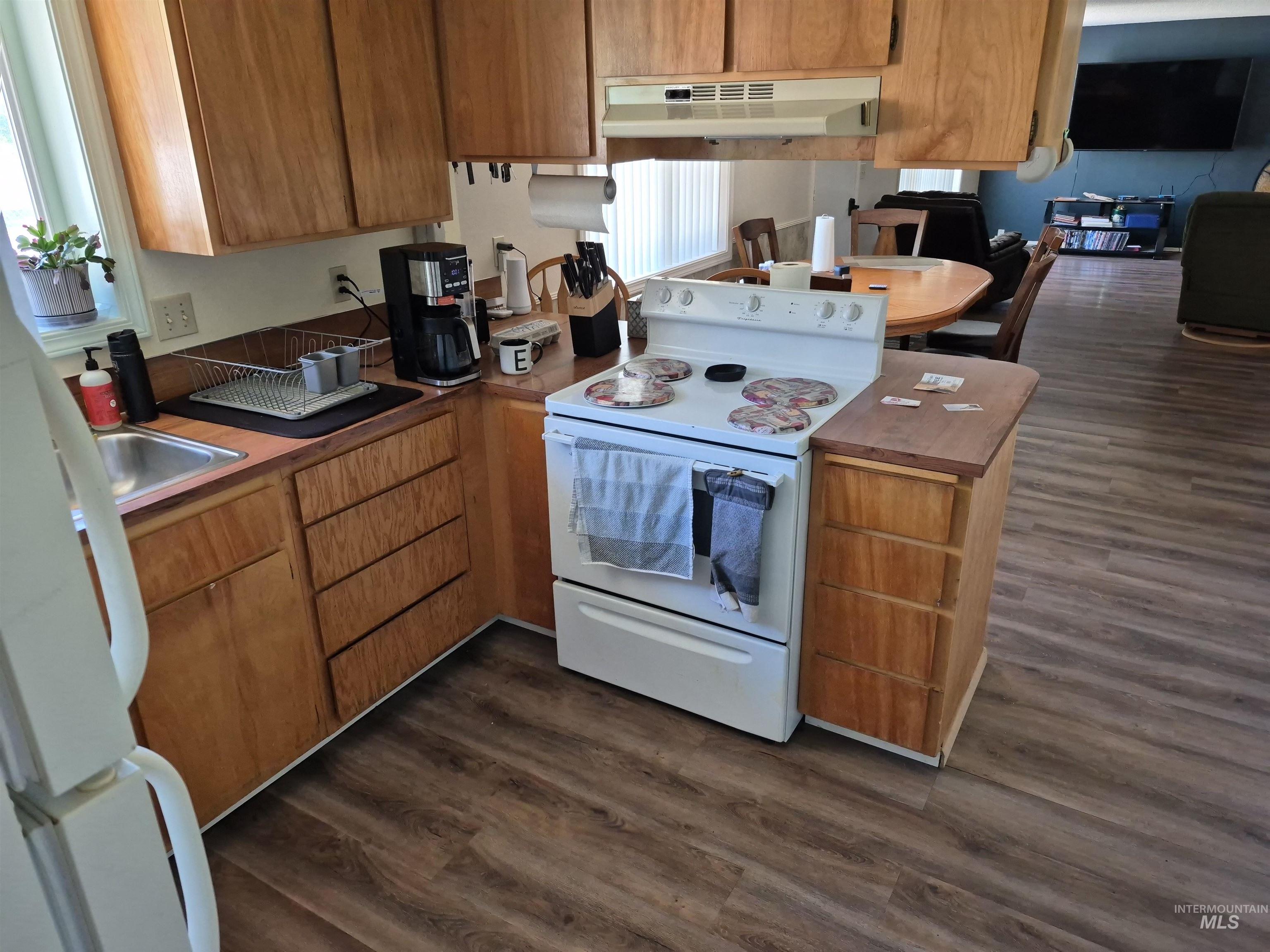 701 Wheeler Street Kendrick, ID 83537 - Photo 8 of 32 Kitchen with dark wood-style flooring, white appliances, brown cabinets, and under cabinet range hood