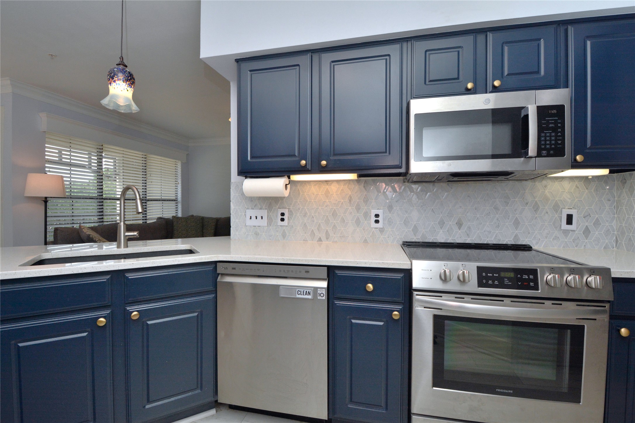 7701 Rialto Boulevard, Unit 124 Austin, TX 78735 - Photo 7 of 22 Kitchen featuring blue paneled cabinetry with gold-tone hardware, stainless steel appliances, white countertops, and a decorative tile backsplash