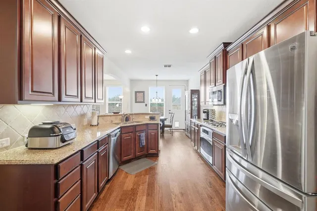 a kitchen with stainless steel appliances granite countertop a refrigerator a sink dishwasher a stove and a dining table with wooden floor