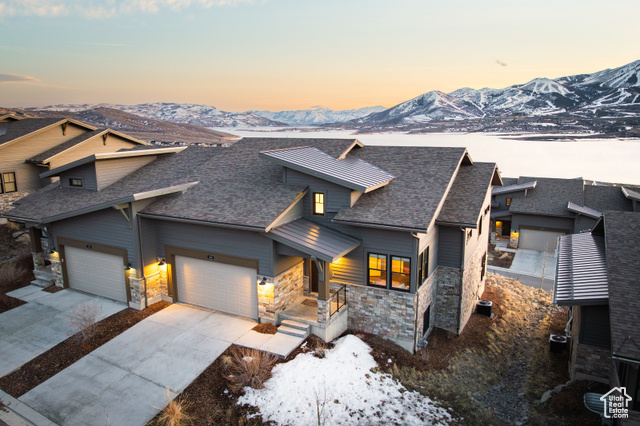 View of front of property featuring stone siding, a garage, concrete driveway, roof with shingles, and a mountain view