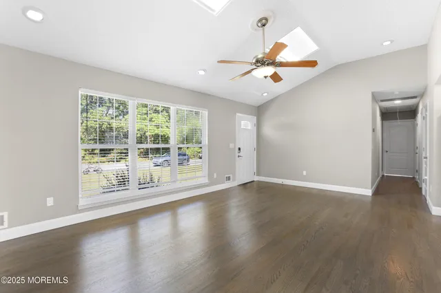 an empty room with wooden floor fan and windows