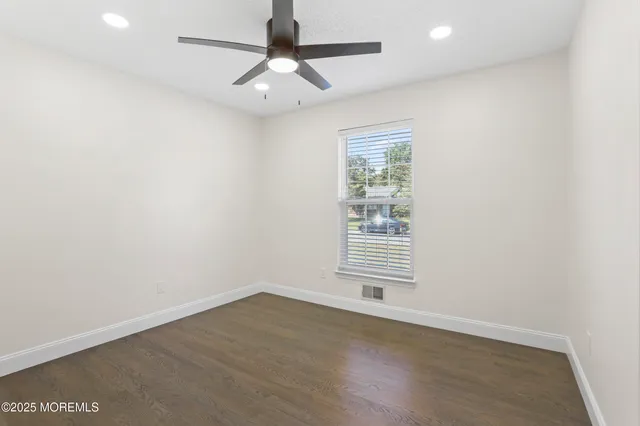 an empty room with wooden floor ceiling fan and windows