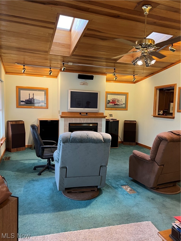 Carpeted living room with crown molding, wooden ceiling, ceiling fan, a tiled fireplace, and a skylight