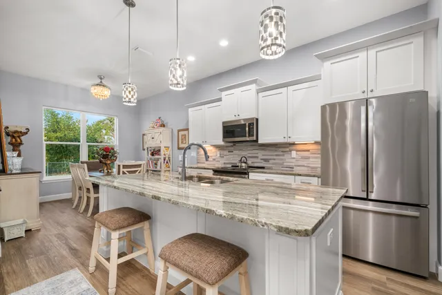 a kitchen with kitchen island granite countertop stainless steel appliances a table chairs sink refrigerator and microwave