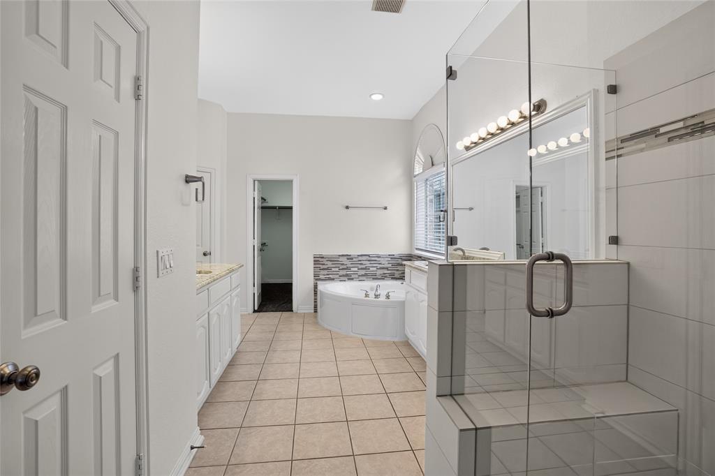 111 Ripplewood Coppell, TX 75019 - Photo 19 of 34 Spacious bathroom featuring a frameless glass shower with built-in bench, corner soaking tub, dual vanity with undermount sinks and granite countertops, and tile flooring