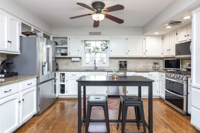 a kitchen with stainless steel appliances granite countertop a dining table chairs refrigerator and cabinets