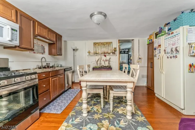 a kitchen with stainless steel appliances granite countertop a stove a refrigerator a oven a white table and chairs with wooden floor