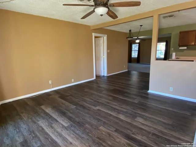 a view of an empty room with wooden floor and a ceiling fan