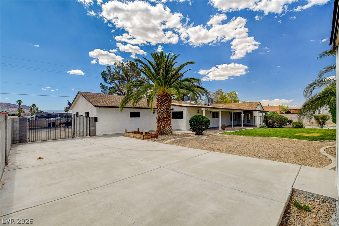 1810 Pinto Road Henderson, NV 89002 - Photo 50 of 53 A spacious concrete driveway leads to a classic home with mature landscaping under a brilliant sky.