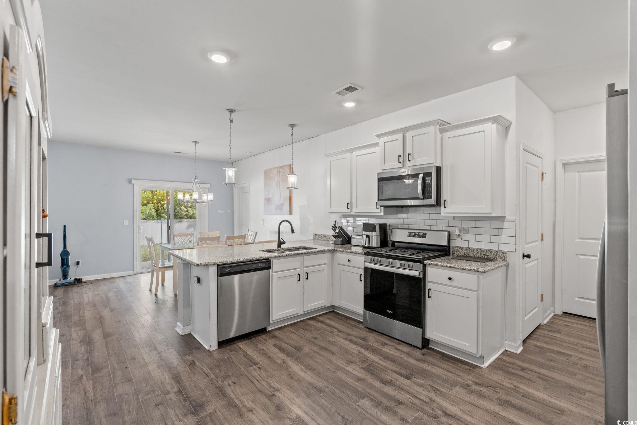 Kitchen with a peninsula, stainless steel appliances, white cabinetry, tasteful backsplash, and recessed lighting