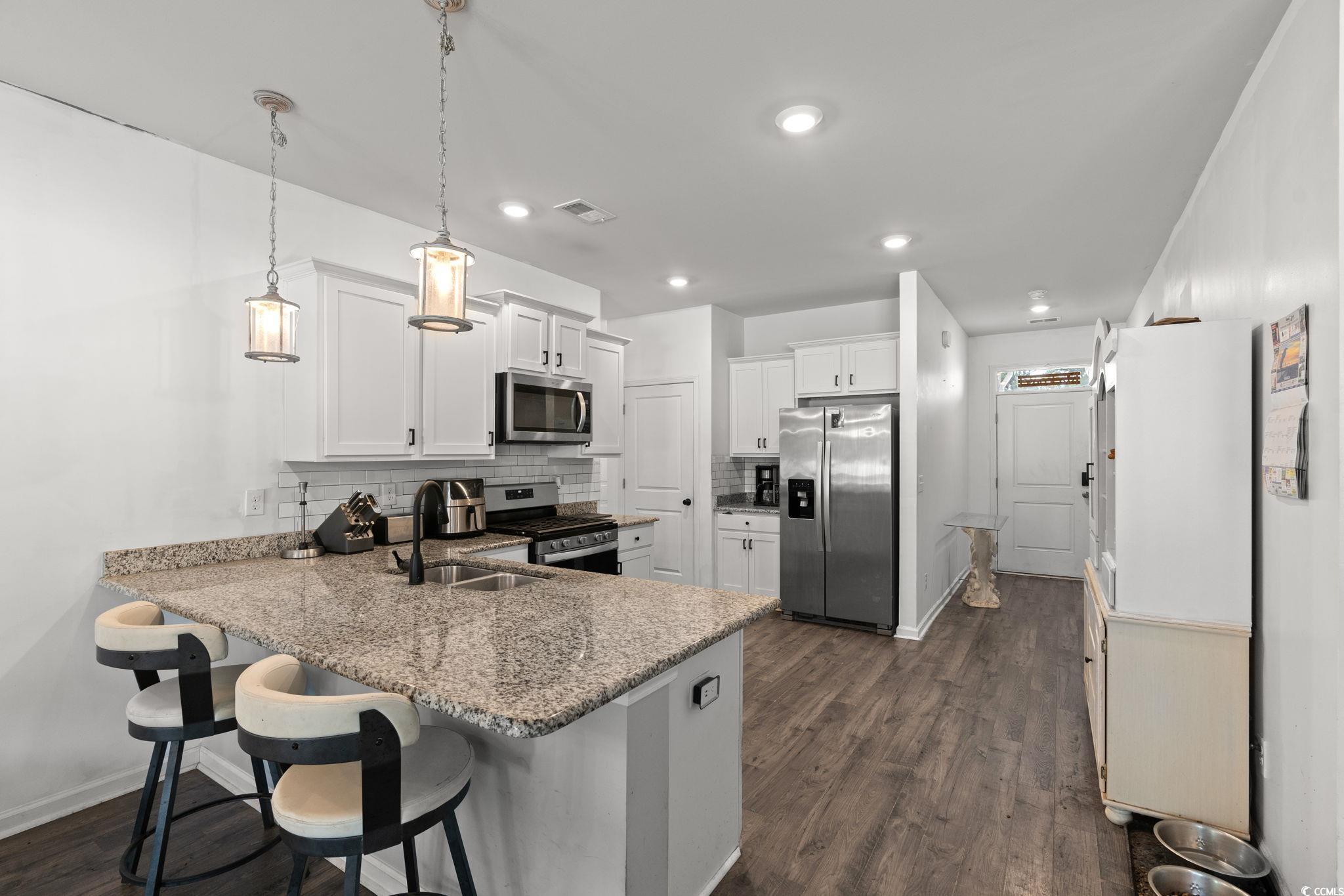 Kitchen with decorative backsplash, a peninsula, stainless steel appliances, white cabinets, and a breakfast bar
