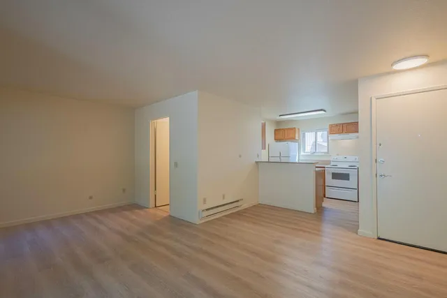 an empty room with a wooden floor and a kitchen