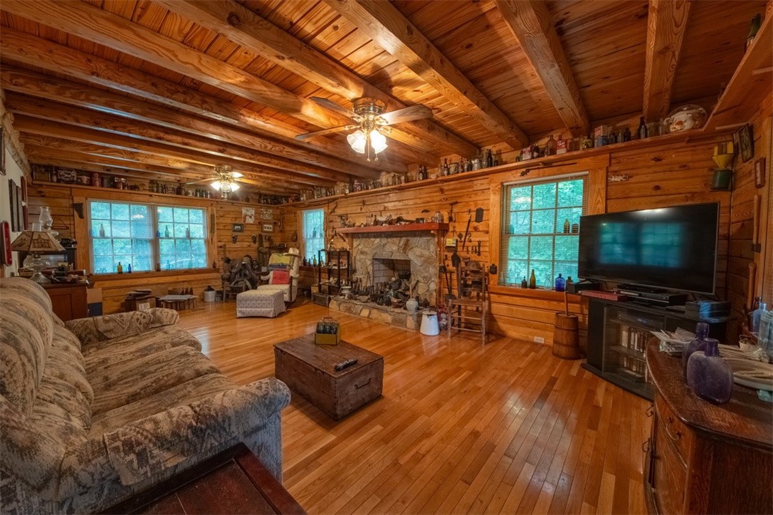 846 Twiggs Ferry Road Hartfield, VA 23071 - Photo 19 of 28 Living room featuring hardwood / wood-style flooring, ceiling fan, wood walls, a stone fireplace, and a wooden ceiling with exposed beams