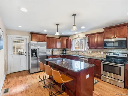 a kitchen with stainless steel appliances granite countertop a sink a stove a refrigerator cabinets and a dining table