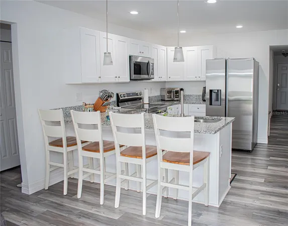 a kitchen with stainless steel appliances kitchen island granite countertop a dining table chairs refrigerator and sink